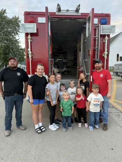 Adults and children stand on the street, a fire engine parked behind them.