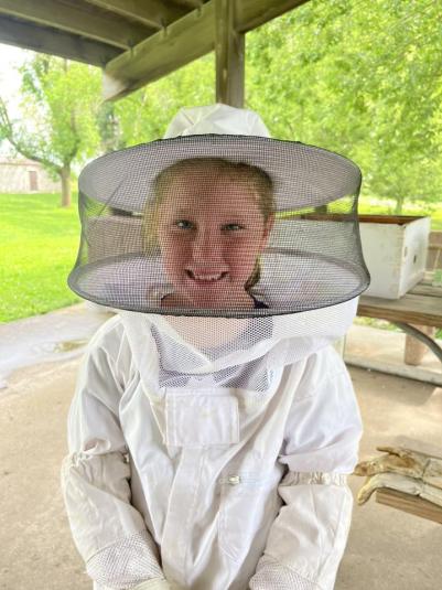 A close-up shot of a girl standing outside, wearing a white beekeeper suit.