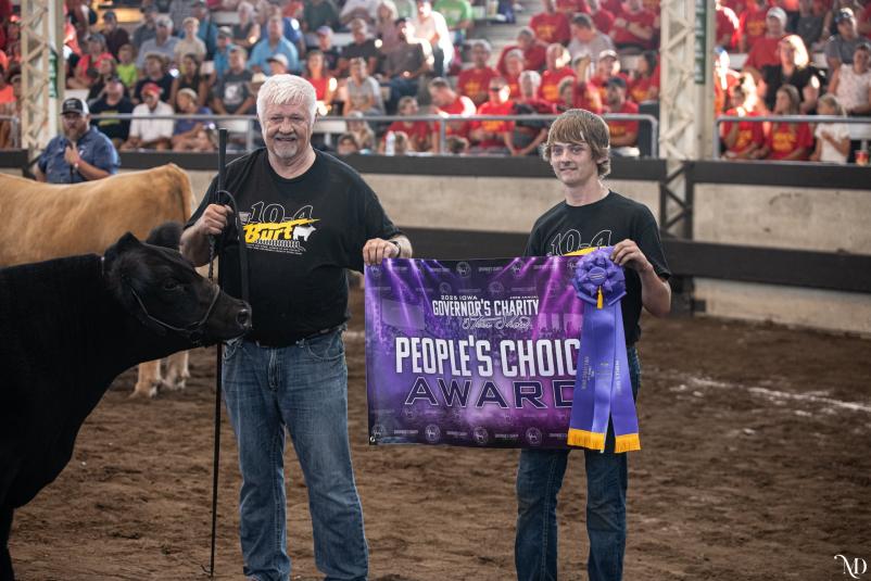 Tucker stands in the show ring with his steer. He and another man are holding up a banner that reads, "People's Choice Award."