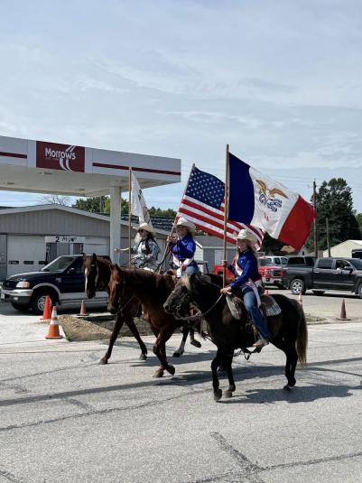 Three women ride on horseback, carrying flags.