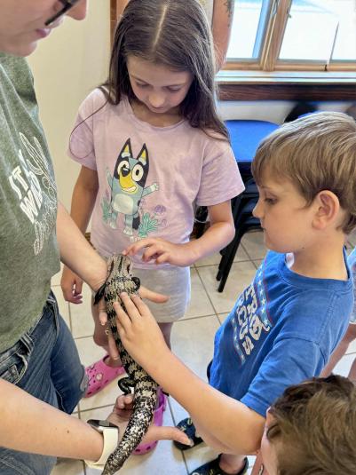A woman holds a reptile while a boy and girl look on and pet the animal.