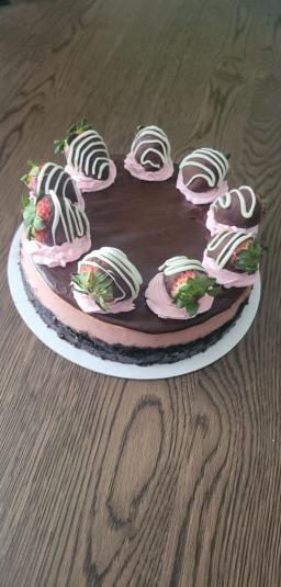 A 9-inch circular cheesecake with a chocolate crust, pink filling, and chocolate frosting, topped with several chocolate covered strawberries.