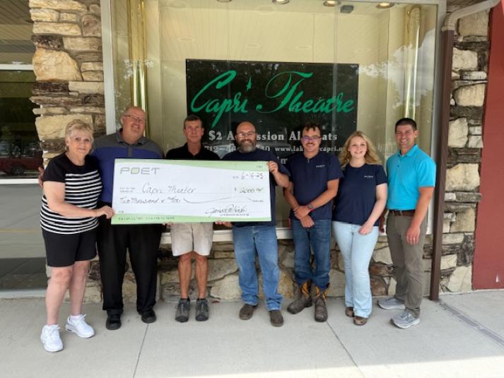 Seven people stand outside the Capri Theatre, holding a giant check written out to the Capri Theatre for $2,000.