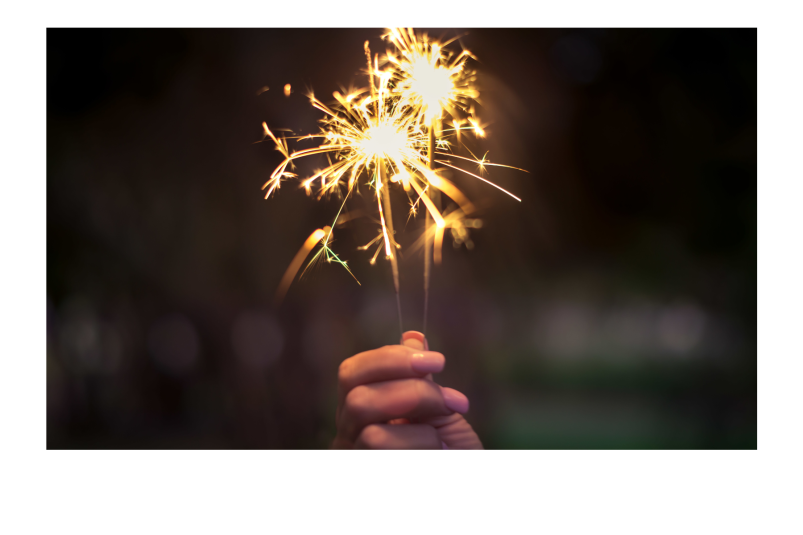 Close-up view of a woman's hand holding a sparkler. Her fingernails are painted pink.