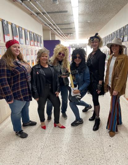 The teachers stand in the school hallway, wearing rock 'n roll themed costumes.