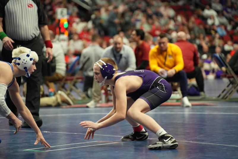 Karson is crouched, facing his opponent. He's wearing a purple wrestling uniform and black shoes with white accents.
