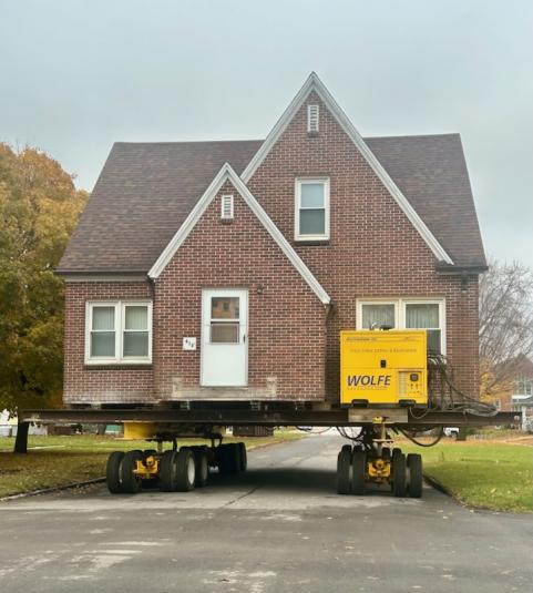 The two story, medium brown brick building is being moved down the street. It is setting on a flatbed trailer.
