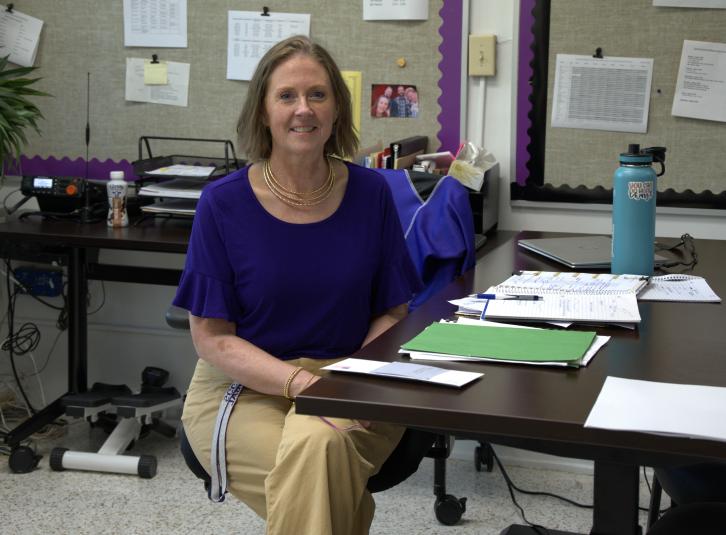 Ms. Pibal sits at her desk. 