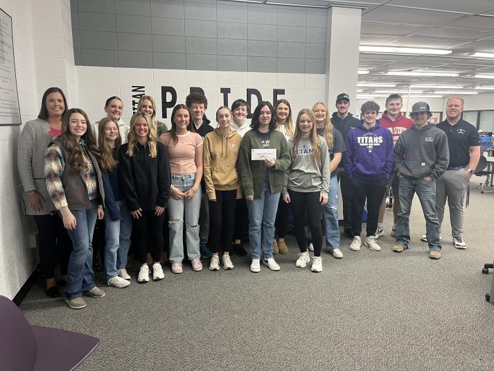 Darci Peterson poses with approximately 15 South Central Calhoun High School students. They are all standing indoors, facing the camera. The carpeting and walls are grey.