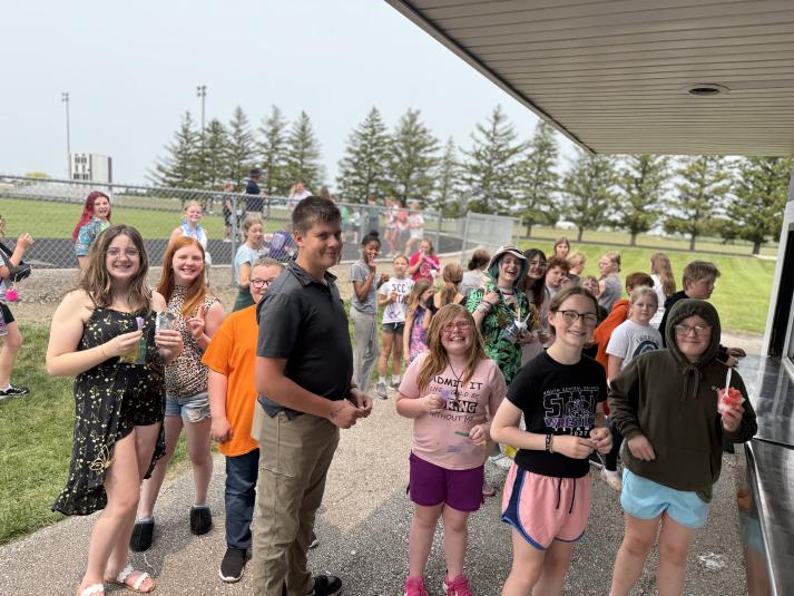 A crowd of middle school students stand outside, in line at the concession stand.