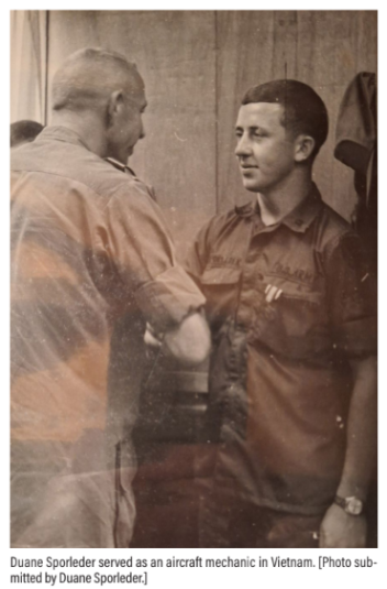 Black and white photo of Duane Sporleder in a military uniform. He is shaking hands with another man who has his back to the camera. 
