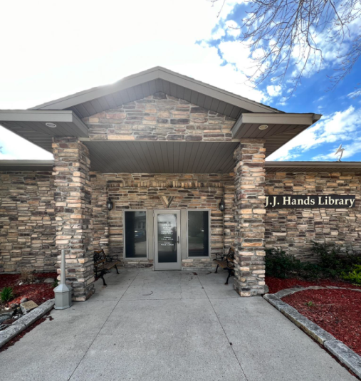 Exterior shot of the J.J. Hands Library in Lohrville, Iowa, a brown, cream, and black one-story stone building.