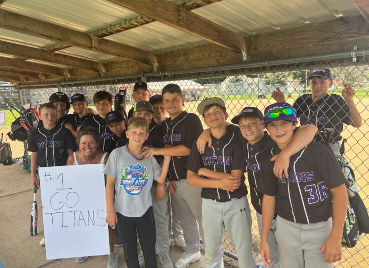 The players stand inside the dugout. A woman holds a sign that reads "#1 Go Titans."