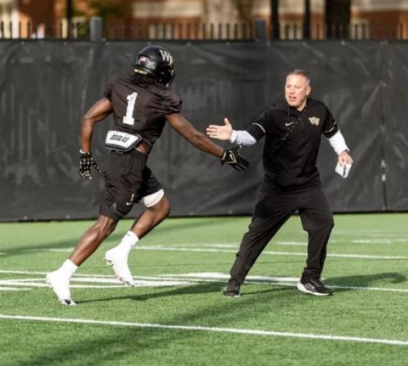 Beschorner is on the field as a player in uniform runs up to him. Both have their arms extended to the other, ready to shake hands.
