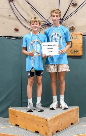 Two boys stand on a podium, wearing matching blue T-shirts.