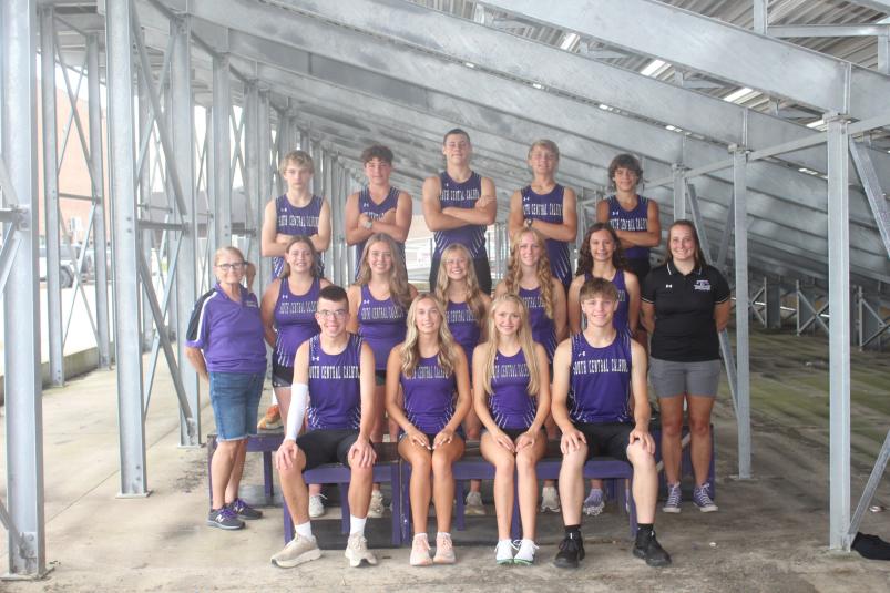 The team poses on benches, underneath the bleachers.
