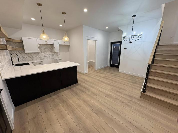 The interior of a finished model home, of the Kitchen and Dining Room area. The floor is a light brown wood floor. The walls, ceiling, and floors are white. 