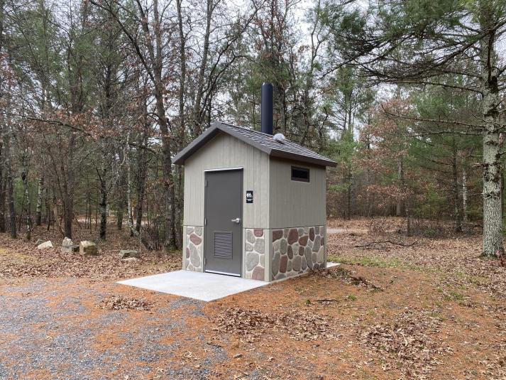 A photo of the exterior of a grey vault toilet. 
